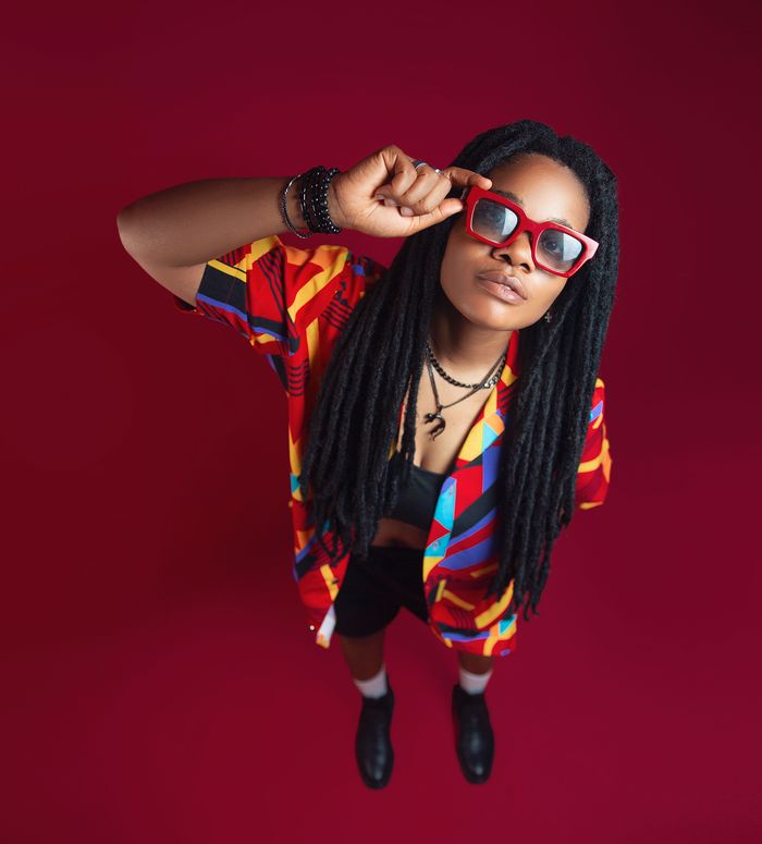 Services Colorful portrait of an adult with long hair and vibrant clothing, set against a striking red background.