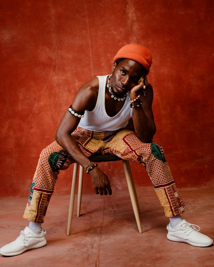 Services Trendy fashion portrait of a man sitting with vibrant pants and accessories in a studio setting.